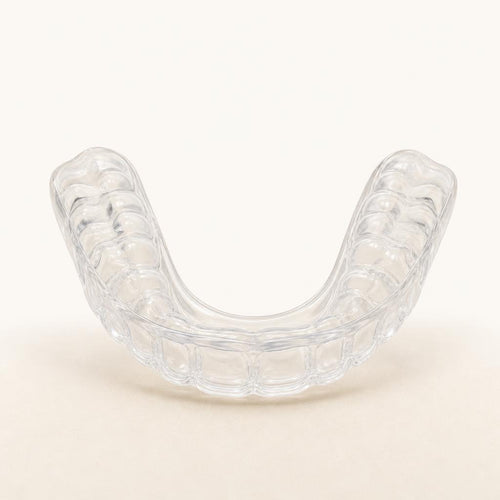Heration night guard, clear moulded dental tray on a warm sand background